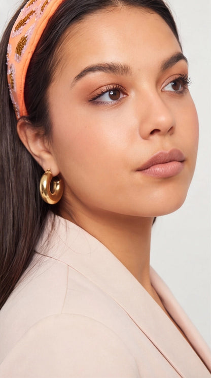 Woman wearing a pink headband and gold earrings against a neutral background