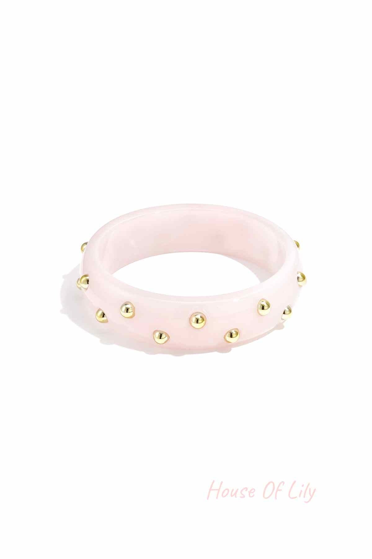 Light pink resin bangle decorated with small gold studs on white background