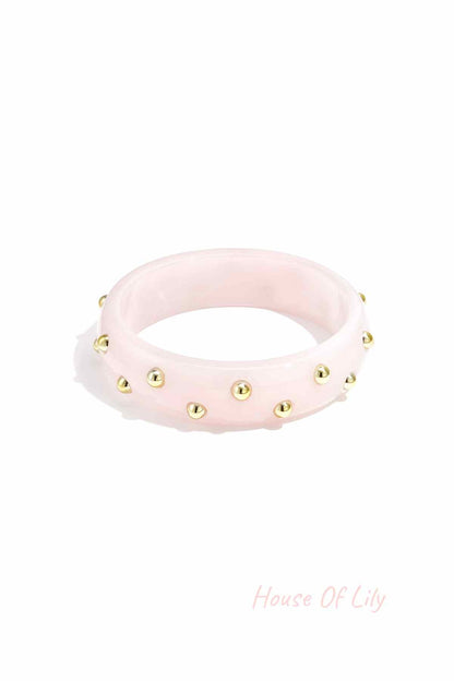 Light pink resin bangle decorated with small gold studs on white background