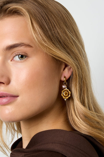 Close-up side profile of woman wearing one artisanal floral charm earring showing gold hoop and ceramic flower with pearl and coral accents