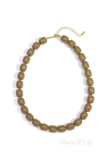 Close-up of coffee brown chunky acrylic bead necklace with gold-tone chain extension on white background