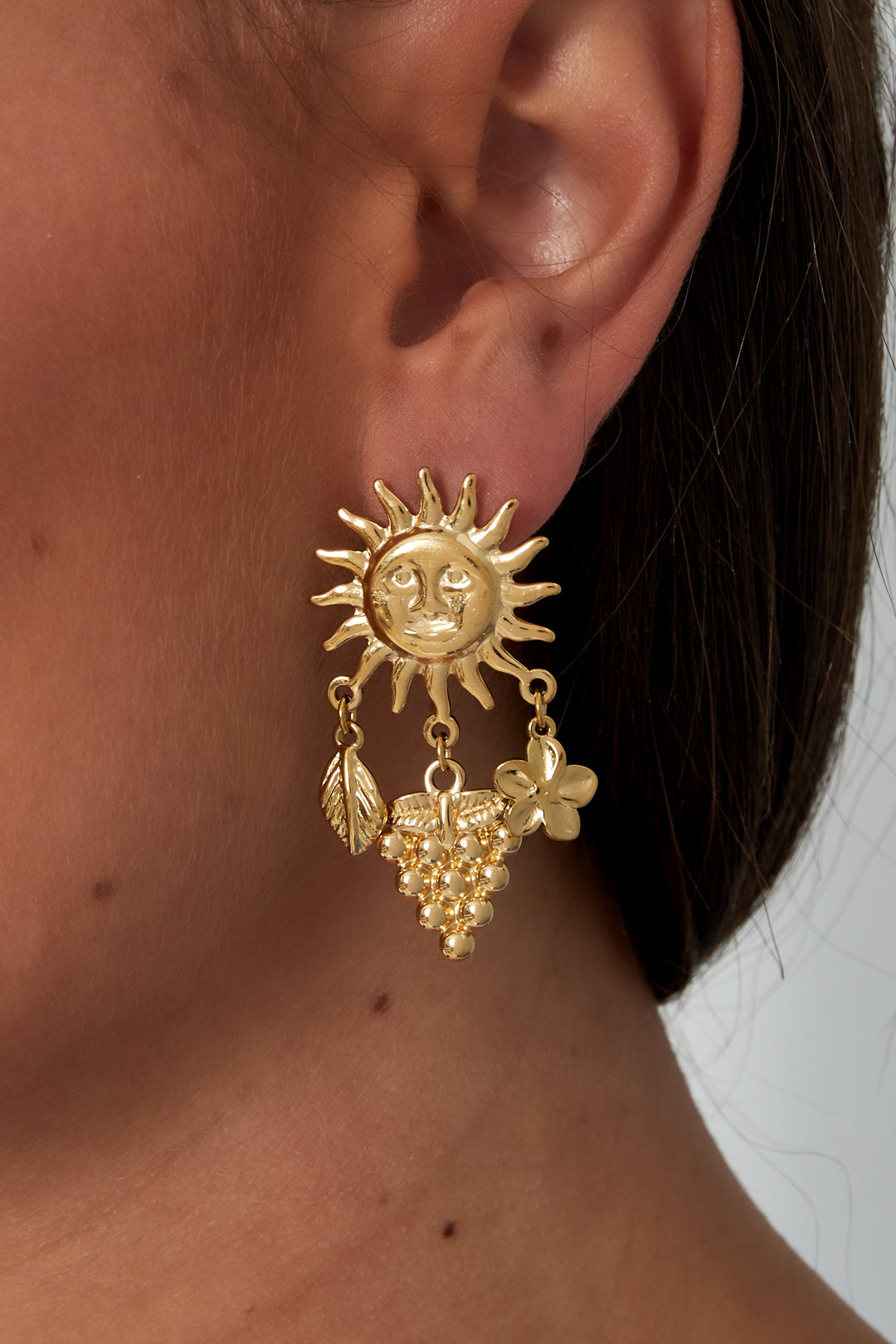 Close-up of gold sun charm drop earring worn on a woman's ear highlighting its sculptural details and youthful design