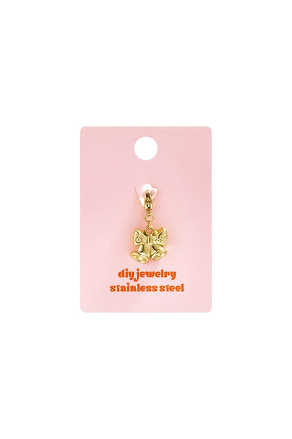 Golden bell charm with a bow, crafted from gold-tone stainless steel, displayed on a pink jewelry backing card.