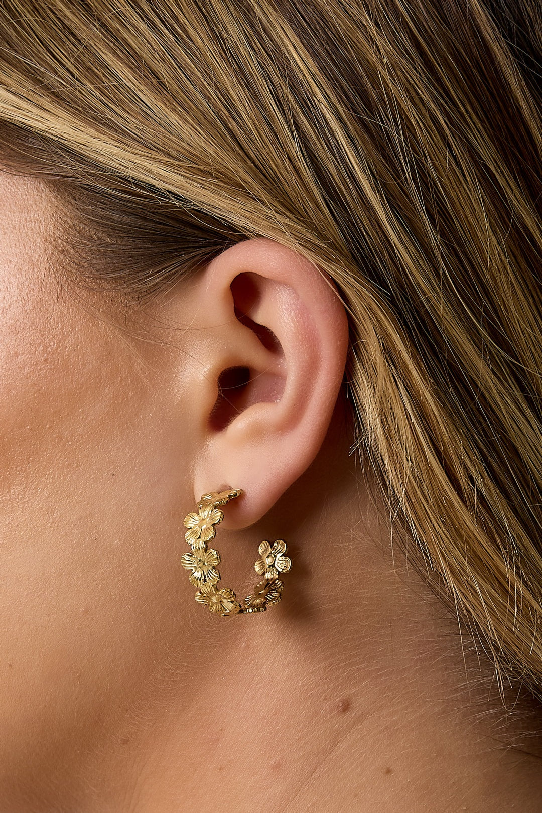 Side profile of a woman wearing gold floral hoop earrings, highlighting their size and how they complement the face.