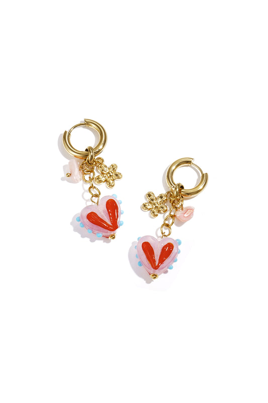 Pair of gold hoop earrings with dangling pink heart charms decorated with red and blue details and small gold flower charms on white background