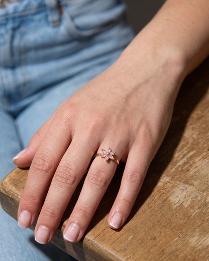 Blooming crystal flower ring with pink marquise-cut stones on a gold band resting on a grey slate surface.