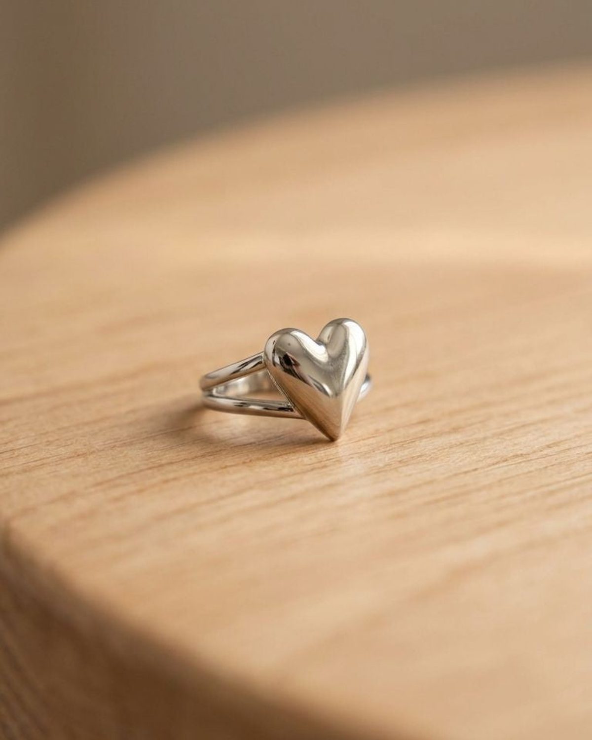 Close-up of oversized puffed heart ring made of polished stainless steel, placed on a wooden surface highlighting its smooth finish and reflections.
