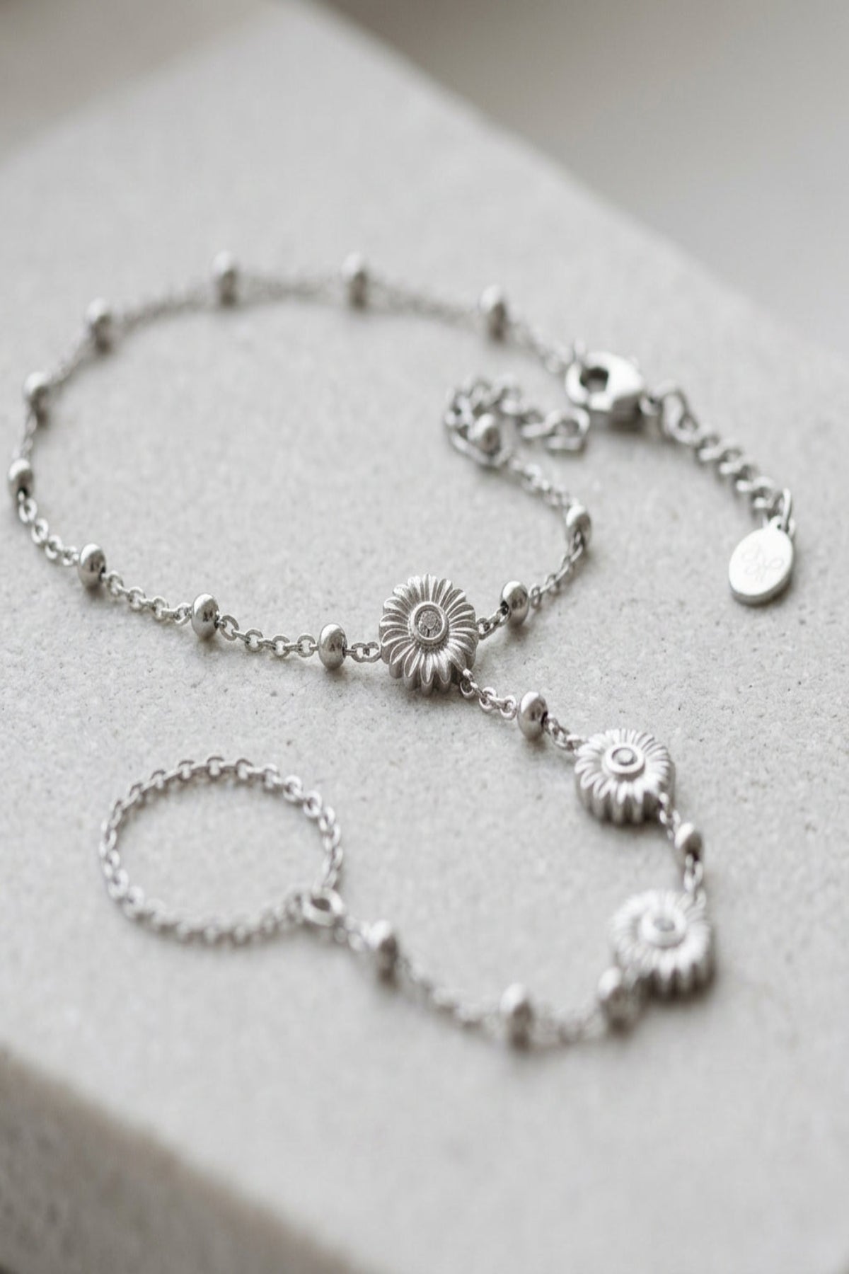 Delicate floral finesse bracelet made of stainless steel with lobster clasp, shown on textured surface highlighting its fine micro-texture and sheen.