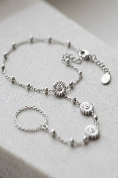 Delicate floral finesse bracelet made of stainless steel with lobster clasp, shown on textured surface highlighting its fine micro-texture and sheen.