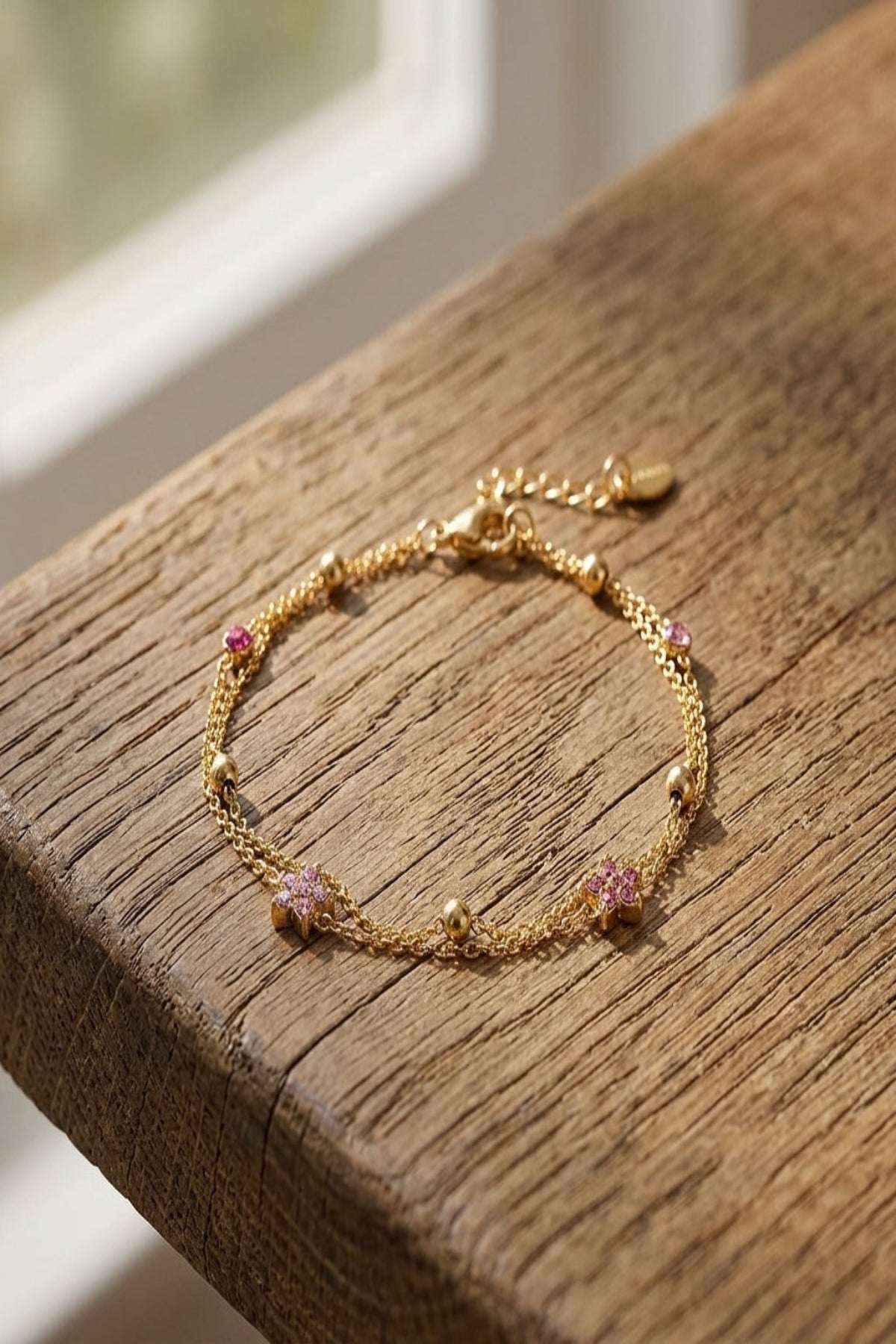 Delicate bracelet featuring colored stones and flower charms with a lobster claw clasp, displayed on a textured wooden surface.