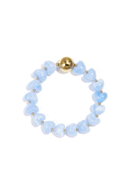 Blue heart-shaped acrylic beaded bracelet with gold bead accent on white background