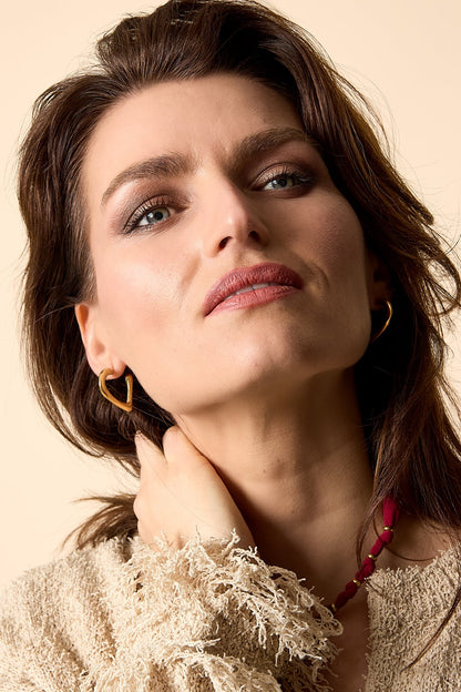 Close-up portrait of woman wearing gold heart-shaped hoop earrings and textured beige top