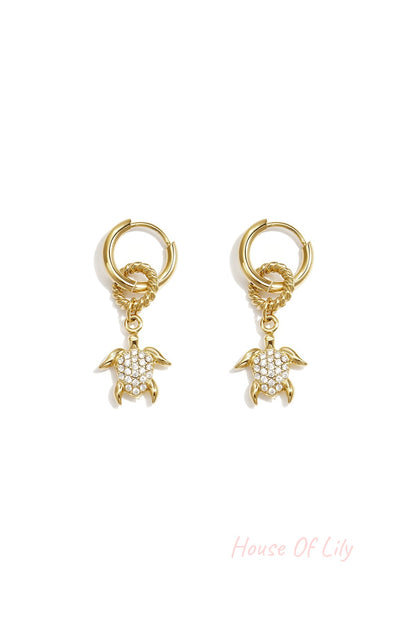 Gold hoop earrings featuring dangling turtle charms with pave crystal shells.