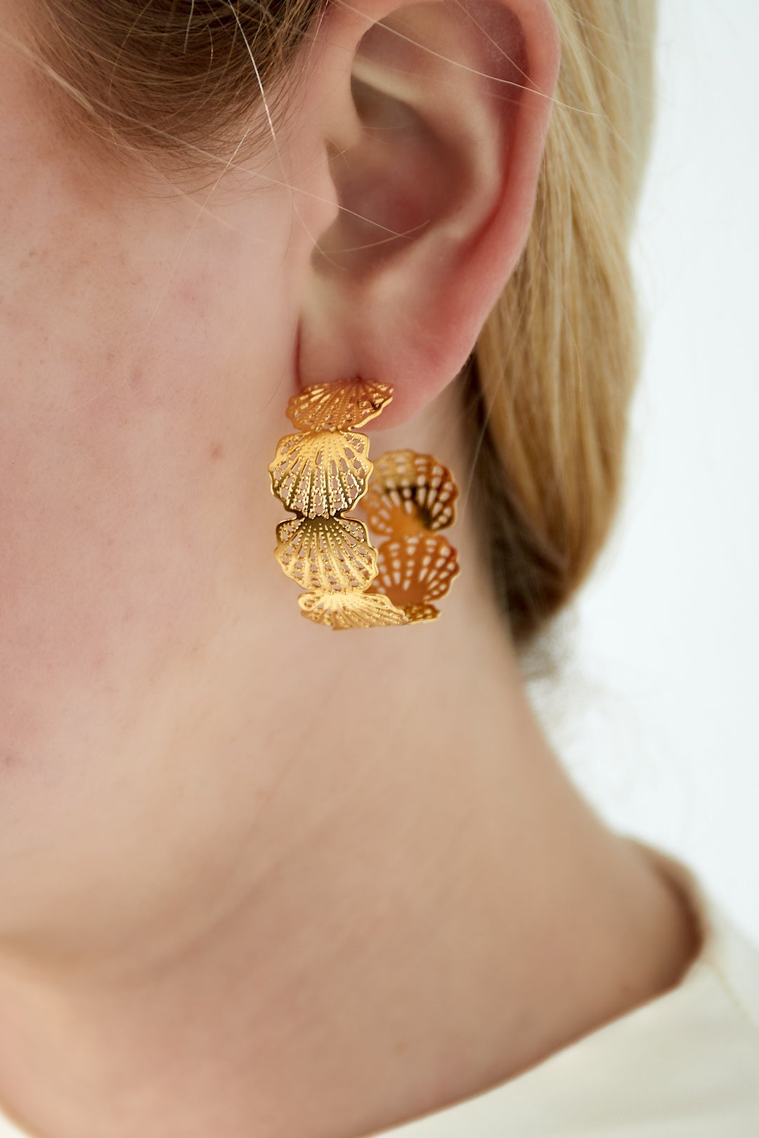 Close-up of a woman wearing gold seashell hoop earrings showcasing their size and intricate design