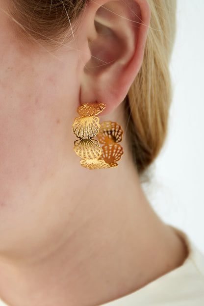 Close-up of a woman wearing gold seashell hoop earrings showcasing their size and intricate design