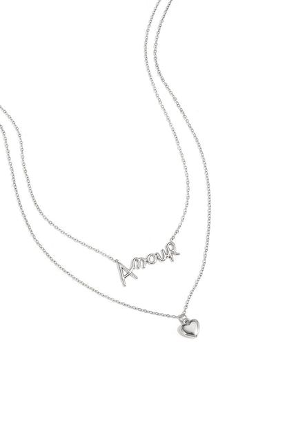 Close-up of silver layered necklace with ‘Amour’ script and heart pendant on white background