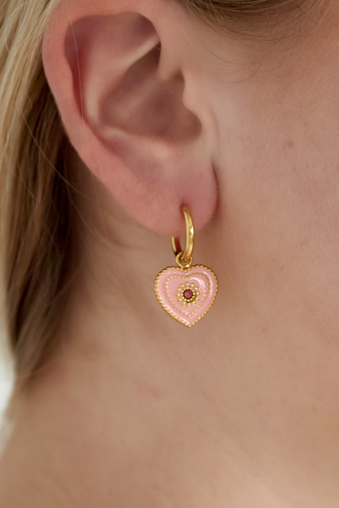 Close-up of ear wearing a gold-tone hoop earring with a soft pink heart-shaped enamel charm and beaded detailing