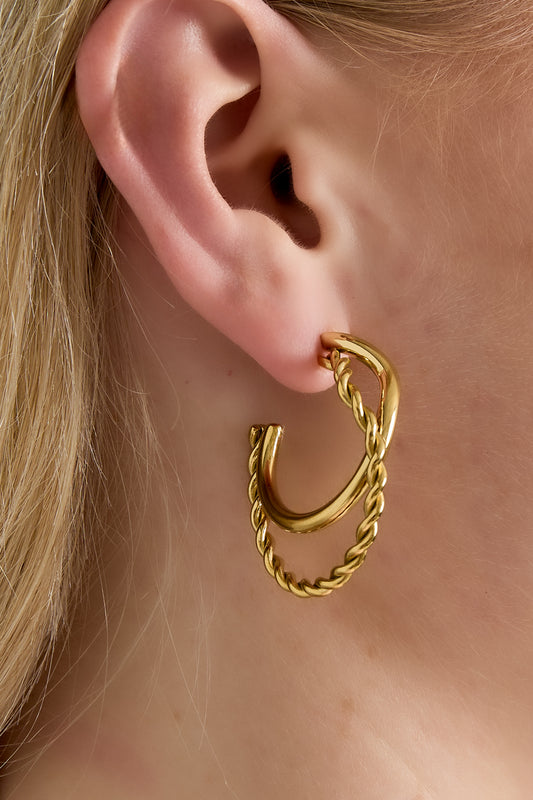 Close-up of a woman's ear wearing gold twist and smooth hoop earrings, showcasing the layered hoop design