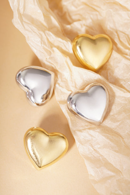 Group of matte gold and silver heart stud earrings arranged on neutral beige paper with texture