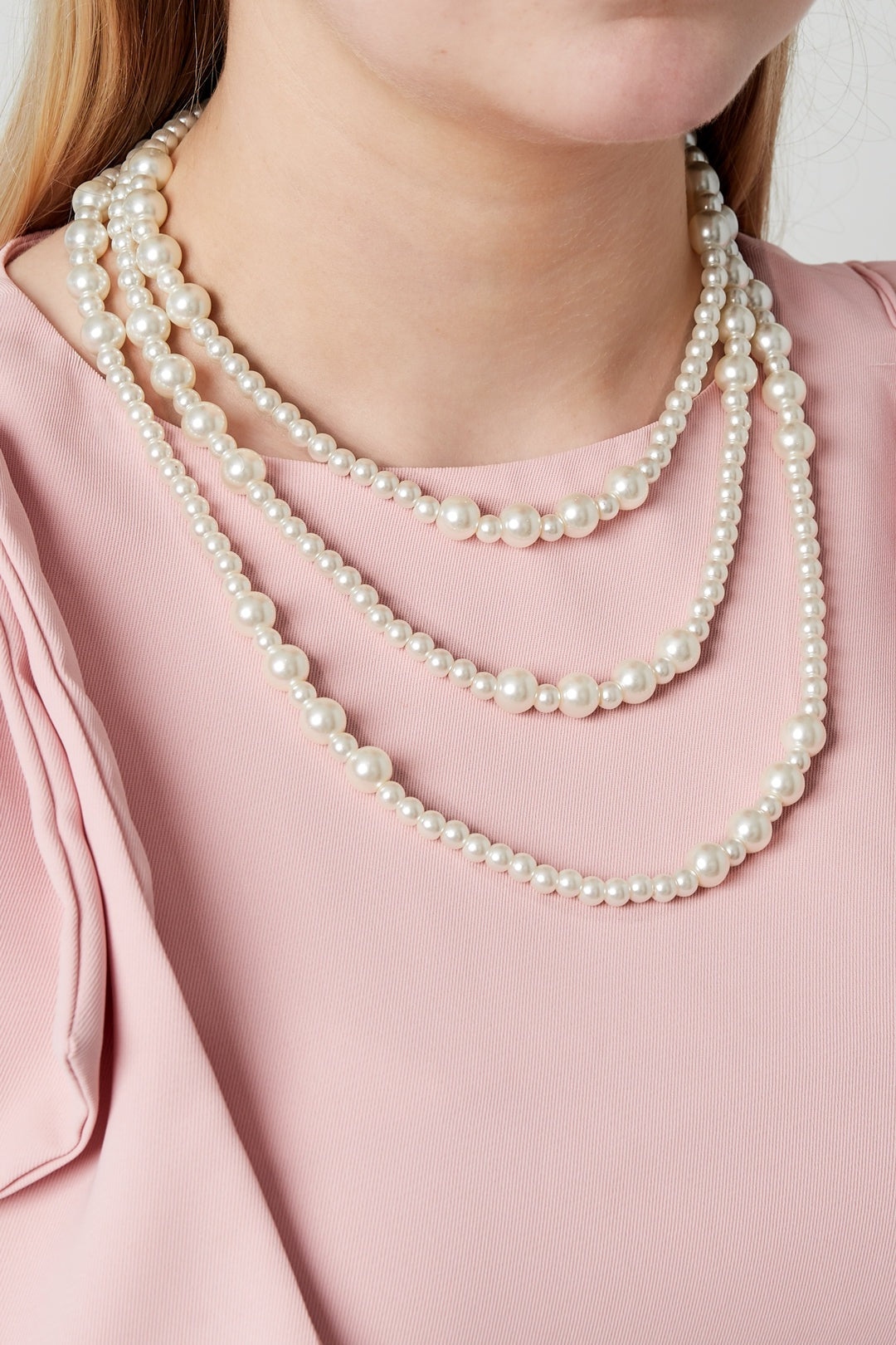 Model wearing a three-layered pearl necklace over a sleeveless pink top showing the necklace’s elegant and youthful style