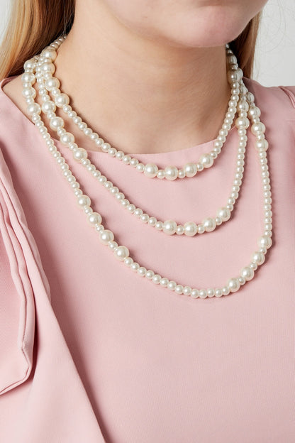 Model wearing a three-layered pearl necklace over a sleeveless pink top showing the necklace’s elegant and youthful style