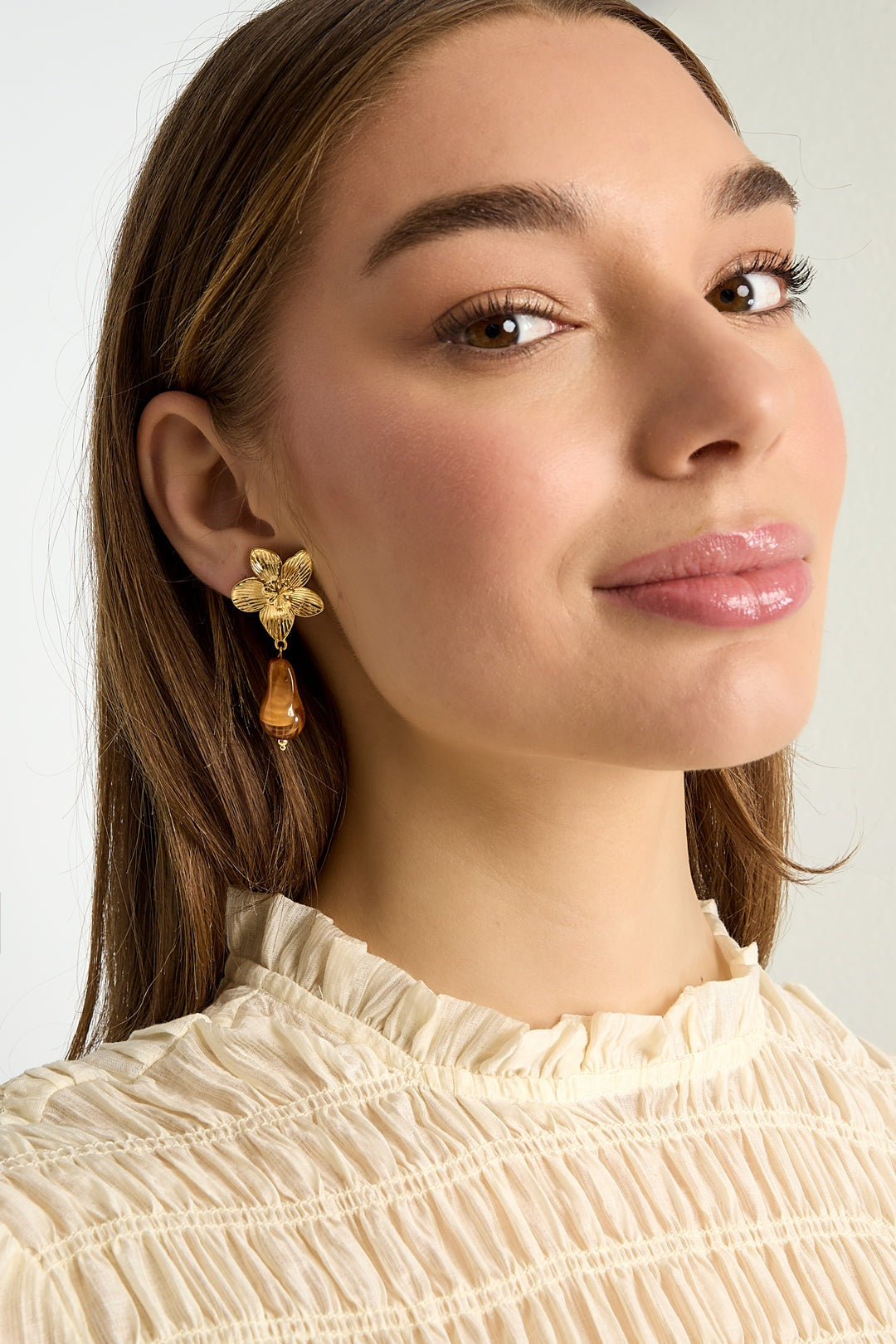 Close-up model portrait wearing gold flower drop earring with amber bead, showcasing design and style
