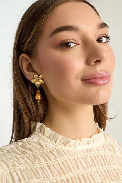 Close-up model portrait wearing gold flower drop earring with amber bead, showcasing design and style