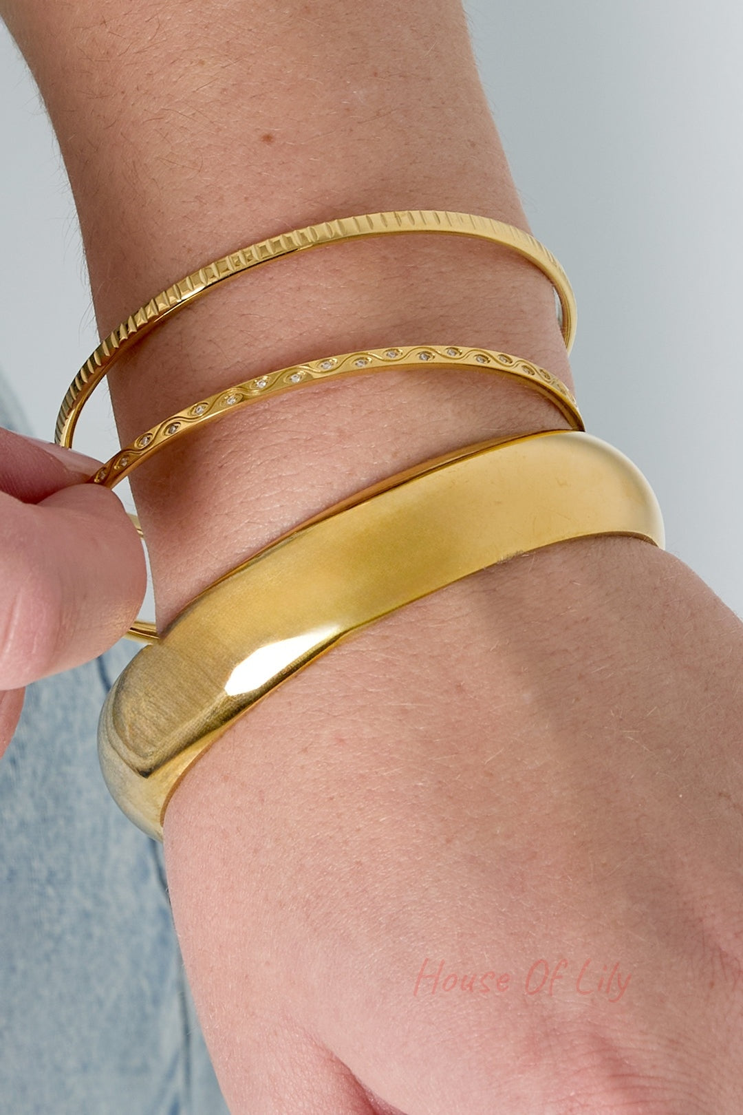 Wrist detail showing multiple gold bangles with textured and smooth finishes