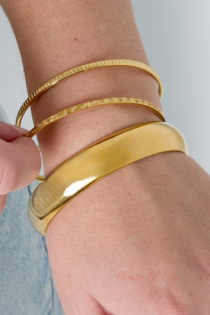 Wrist detail showing multiple gold bangles with textured and smooth finishes