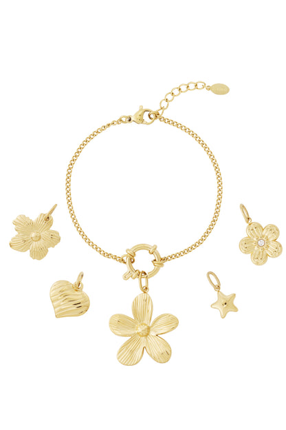 Gold charm bracelet with flower, heart, star, and floral pendants displayed alongside separate charms