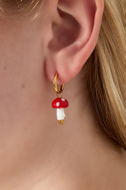 Close-up of a gold hoop earring with red and white mushroom charm worn by woman with blonde hair