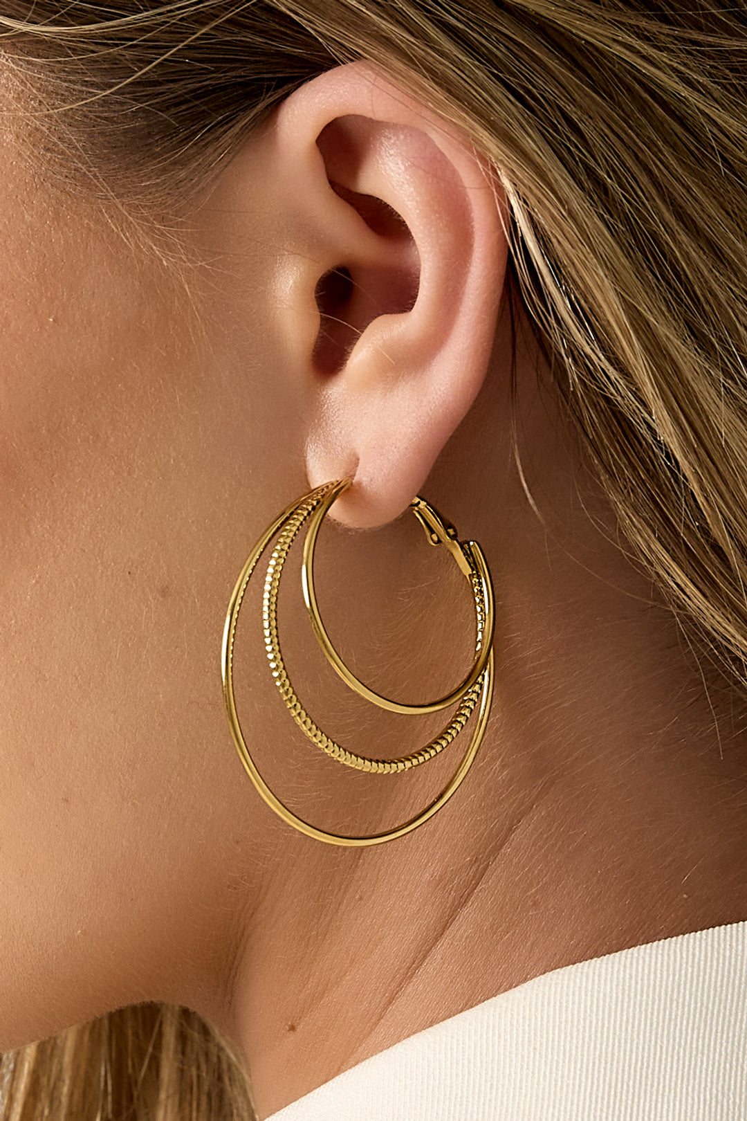 Detailed close-up showing gold triple layered hoop earrings worn on woman's ear highlighting the layered hoops' texture and shine