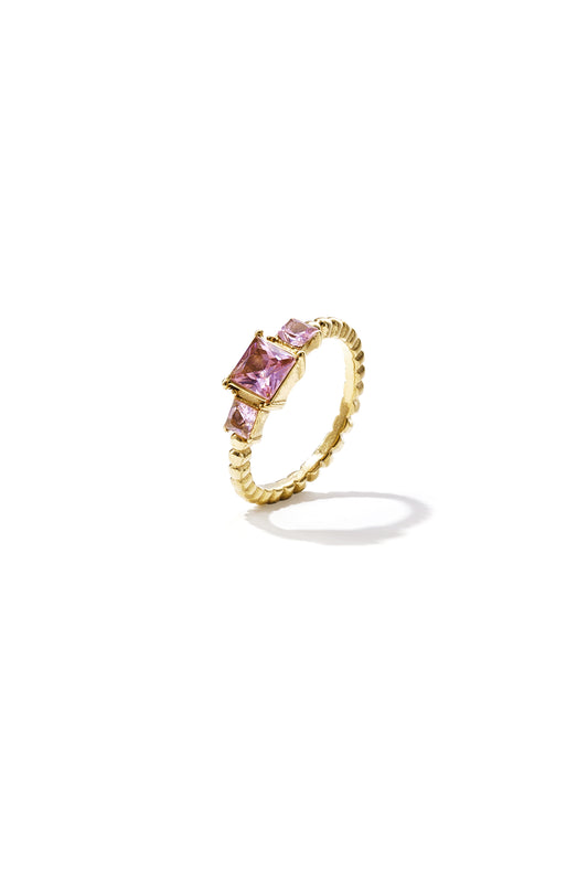 Gold-toned ring with three pink square-cut gemstones and ridged band on white background