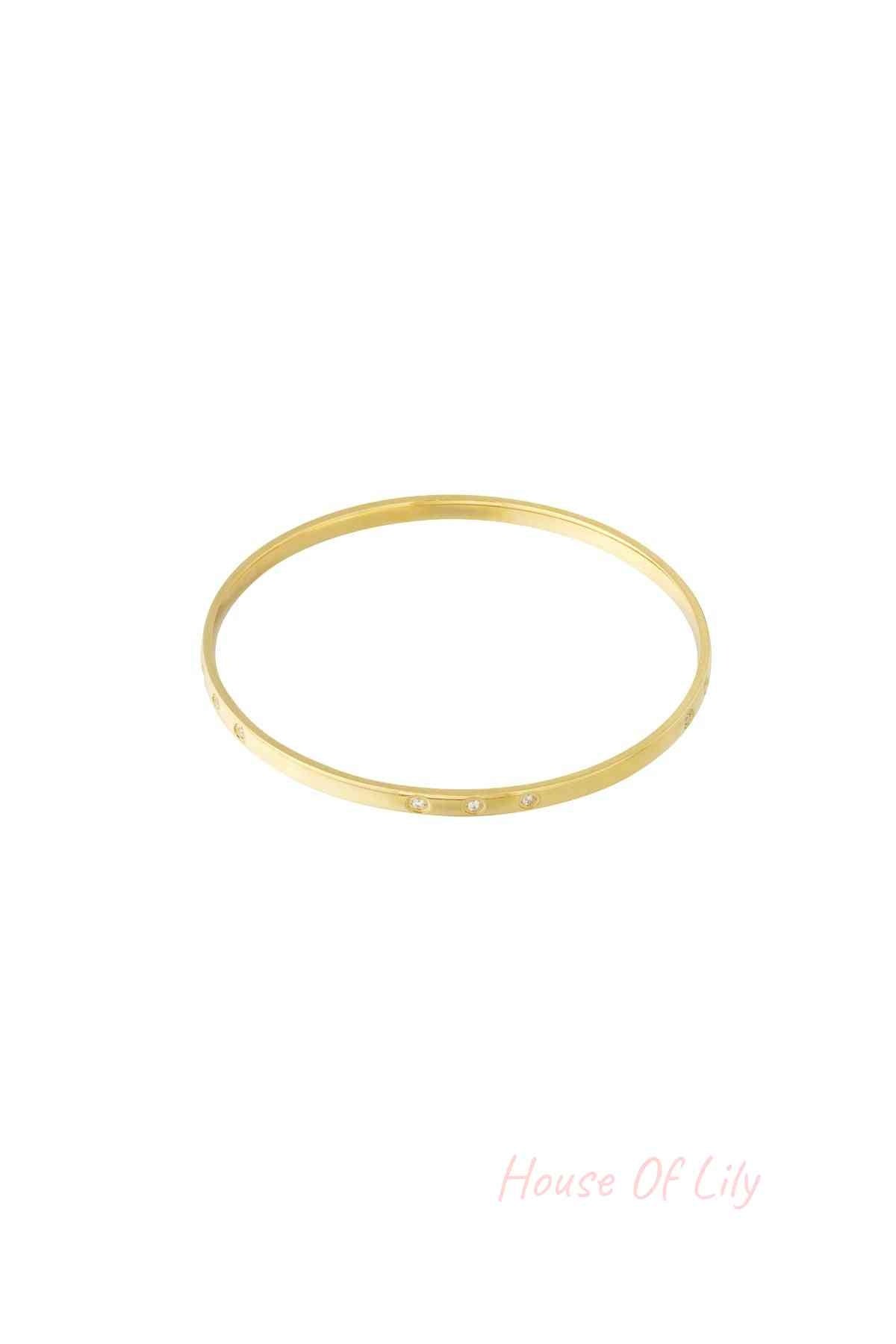 Close-up of a slim gold bangle with small rhinestone accents on a white background