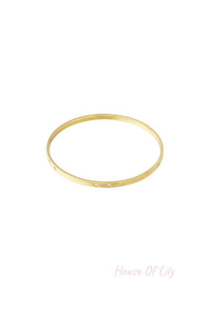 Close-up of a slim gold bangle with small rhinestone accents on a white background