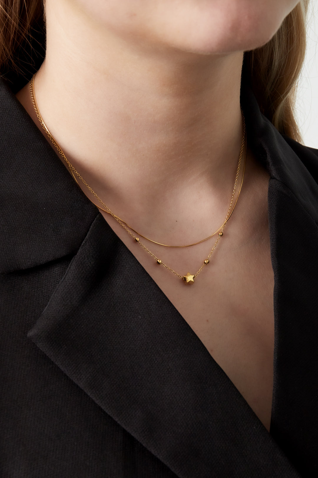 Close-up of model wearing the gold layered star necklace with a black blazer showing soft youthful style