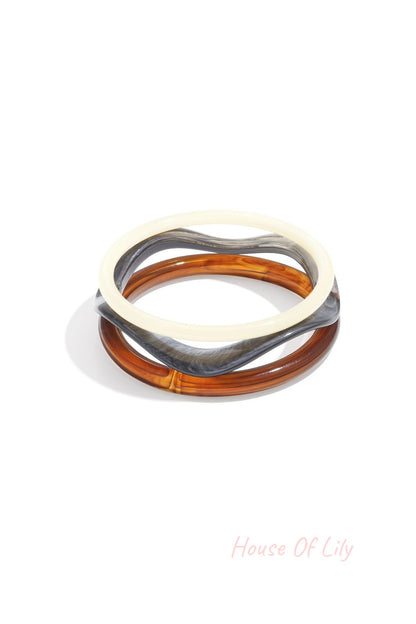 Set of three acrylic bangles in white, tortoise amber, and grey marbled colors on white background