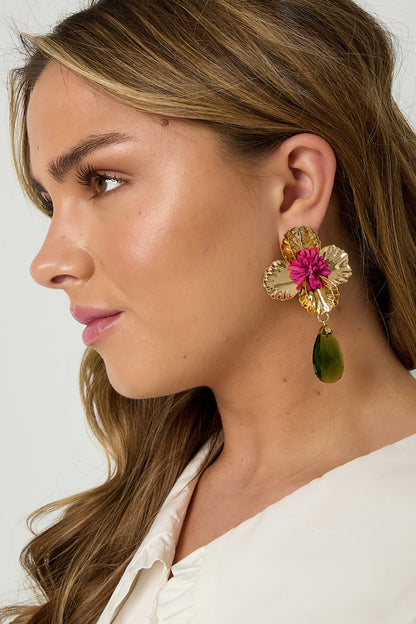 Pair of gold-toned floral drop earrings with deep blue fabric flower center and red faceted teardrop pendants on white background