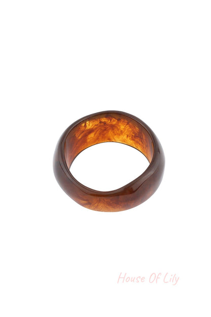 Close-up of dark amber marbled resin bangle bracelet on white background