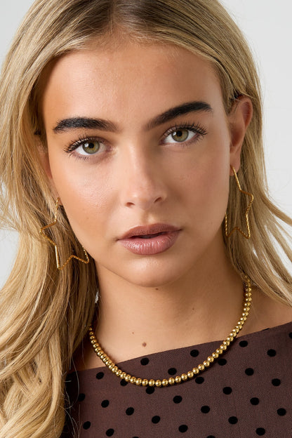 Close-up of a woman wearing gold star-shaped textured hoop earrings and matching gold bead necklace