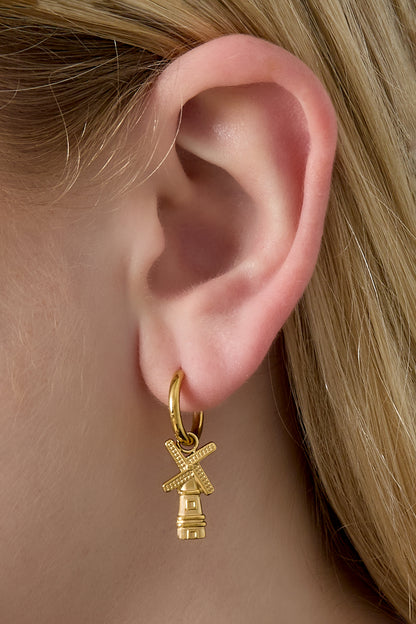 Close-up of gold windmill charm hoop earring worn on a woman's ear showcasing size and fit