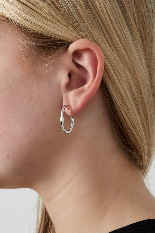 Minimal wave silver clip-on hoop earring worn on model's ear showcasing lightweight design