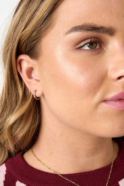Close-up of a woman’s ear and side face wearing the gold hoop earring, showing its dainty sparkle