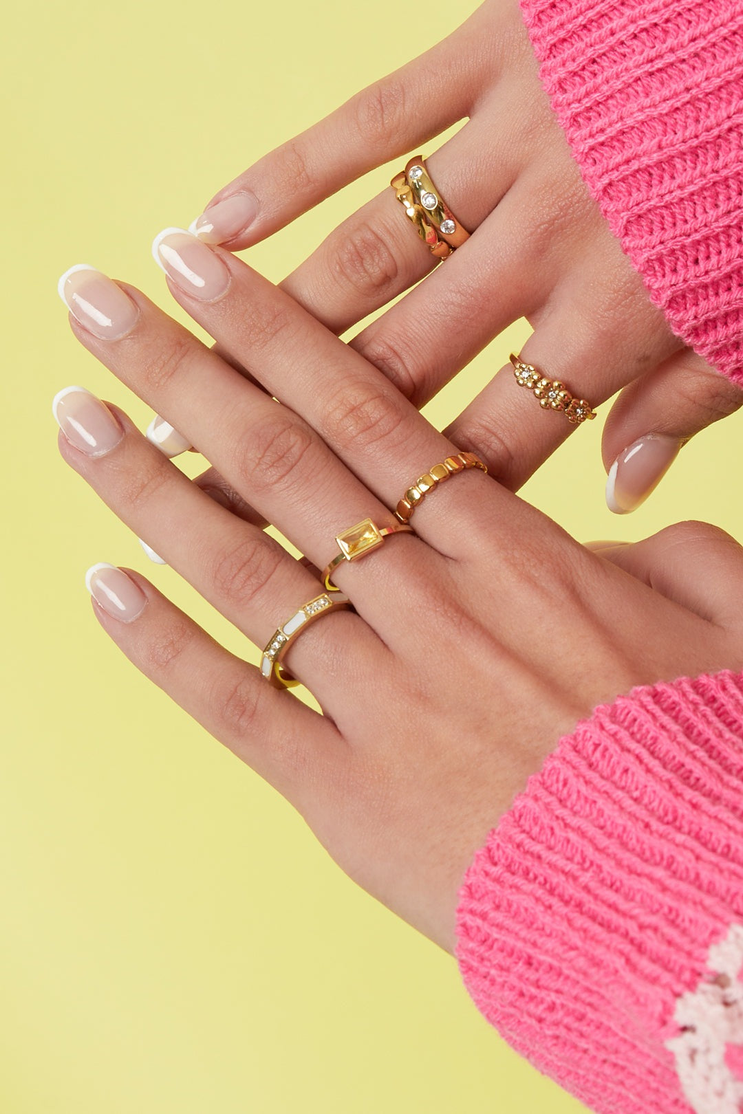Model hand wearing layered gold rings including geometric gold ring with mother-of-pearl and zircon stones, against a yellow background