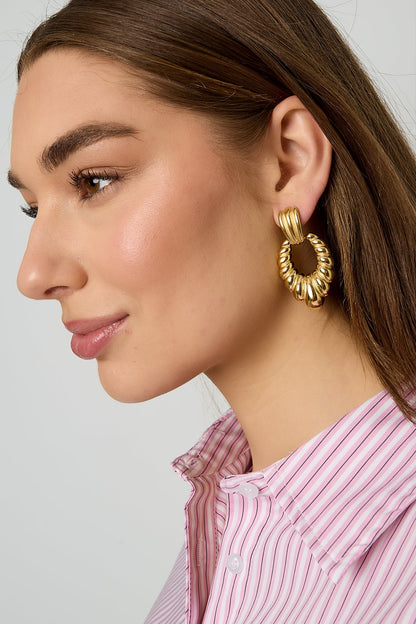 Close-up side profile of model wearing twisted gold hoop earrings showing detailed texture