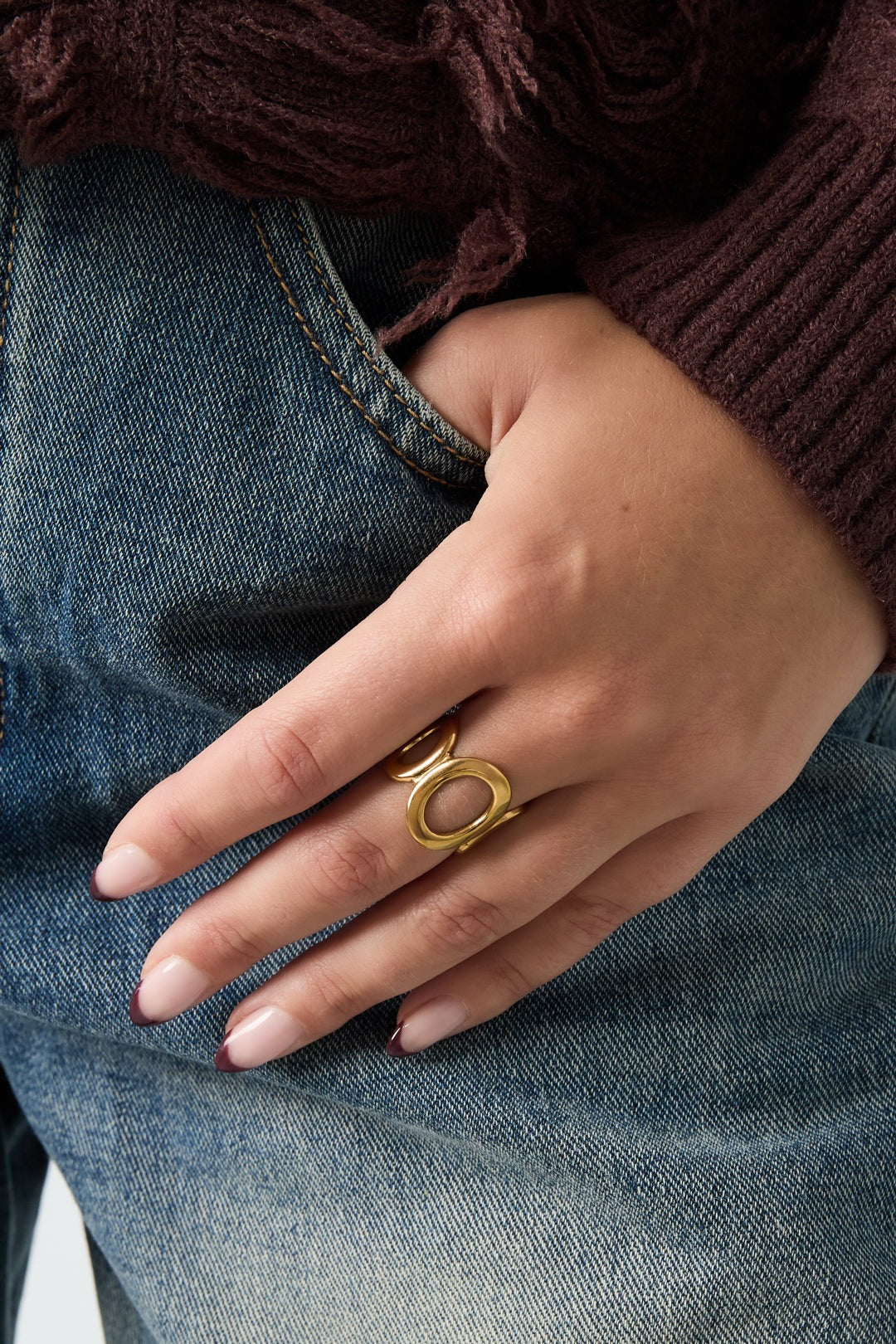 Woman's hand wearing a gold open circle ring styled with casual jeans and a cozy purple sweater
