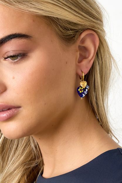 Close-up of woman wearing gold hoop earring with dark blue heart charm and gold heart pendant
