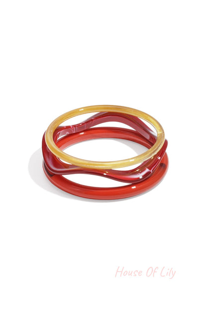 Three wave-shaped acrylic bangles in pink, purple, and amber tortoise shades on white background