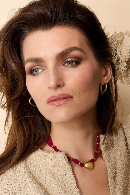 Model wearing gold heart hoop earrings paired with burgundy necklace and neutral textured top