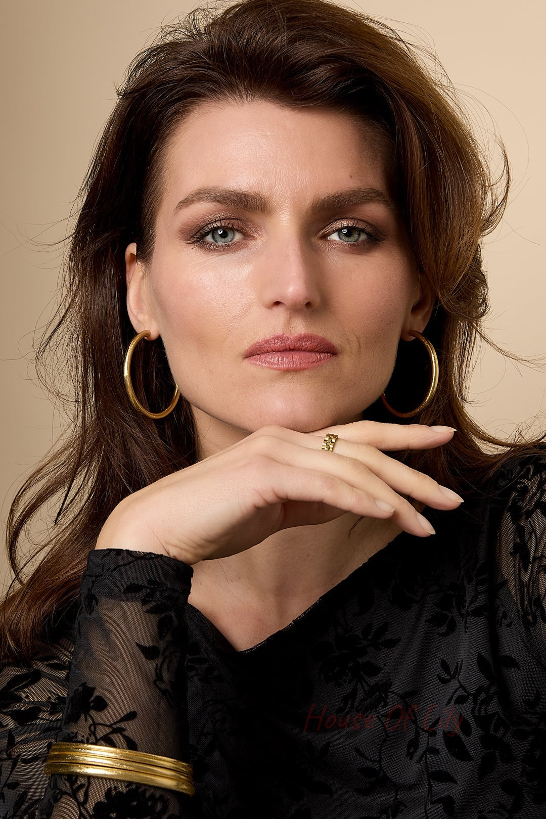 Woman wearing multiple gold circle bangles, including large hoop earrings and a gold ring, styled with a black floral lace top